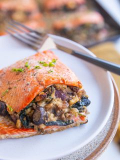 Plate with a stuffed salmon filet on top with a baking sheet of salmon filets in the background.