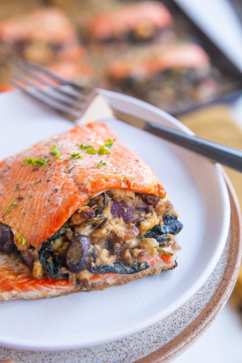 Plate with a stuffed salmon filet on top with a baking sheet of salmon filets in the background.