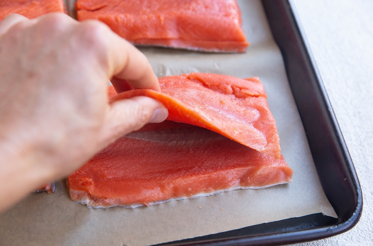 Hand lifting a flap of salmon to expose a pocket for stuffing.