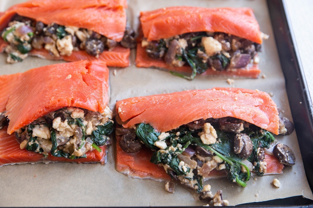 Salmon on a baking sheet stuffed with mushrooms and spinach, ready to be baked.