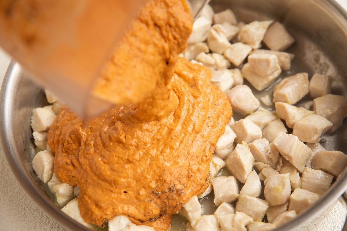 Pouring sundried tomato sauce into the skillet with the chicken.