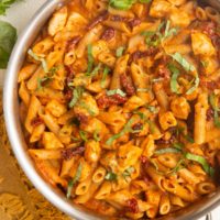 Stainless steel skillet with chicken pasta with sun dried tomato cream sauce.