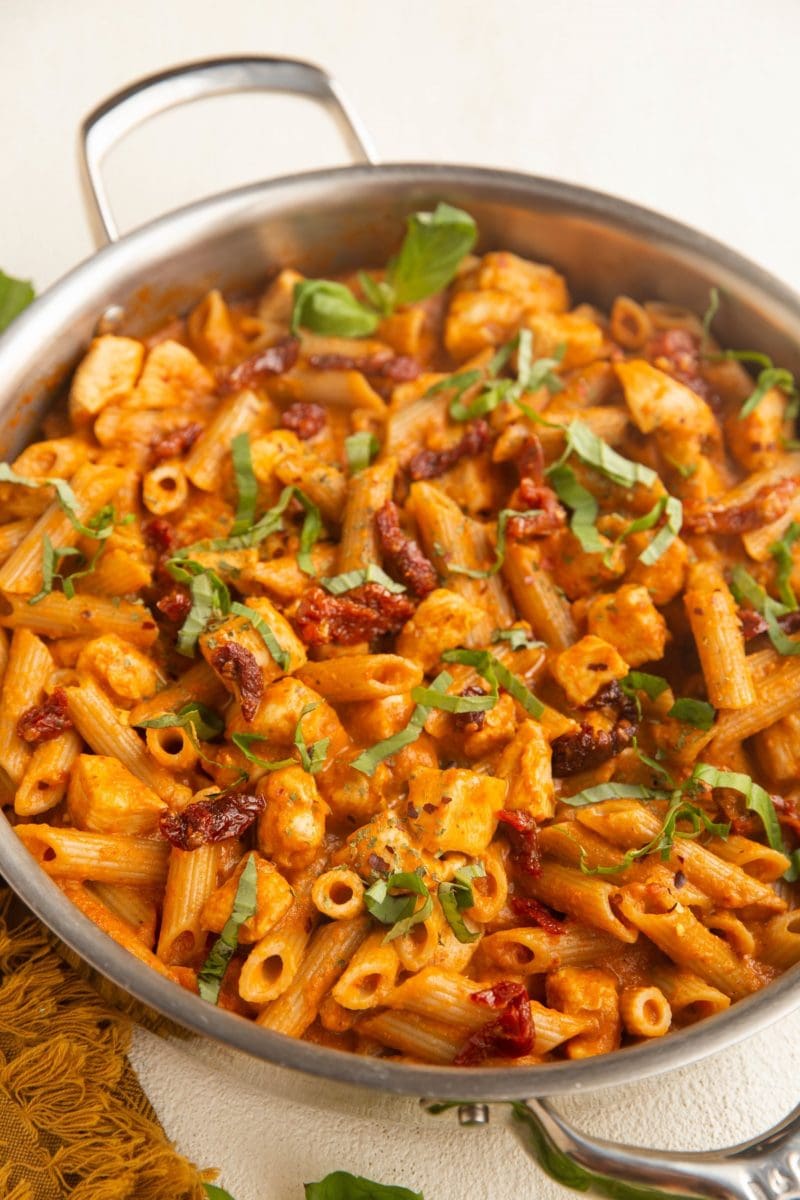 Angled shot of Stainless steel skillet with chicken pasta with sun dried tomato cream sauce.