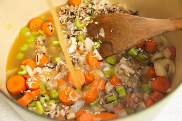 Pouring chicken broth into the pot with the vegetables and rice