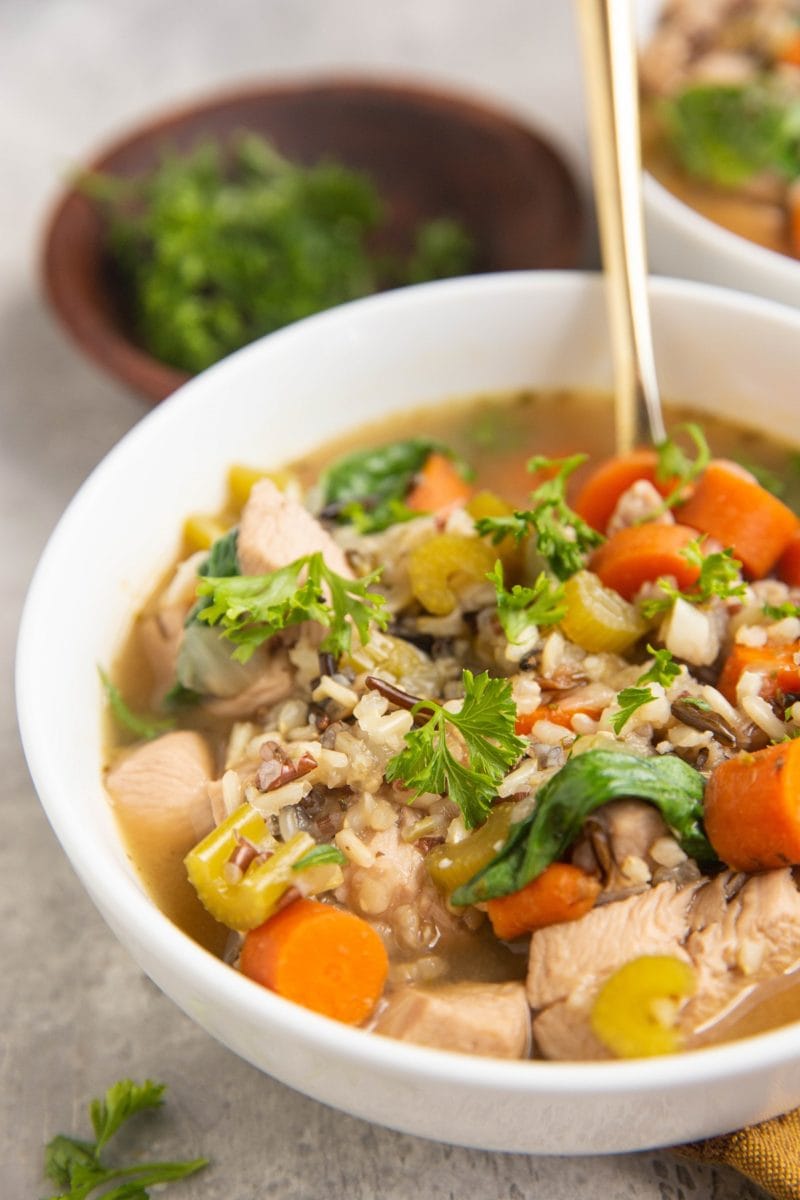 Close up of a white bowl of wild rice chicken soup with a golden spoon inside