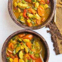 Two wooden bowls of yellow Thai curry soup with chicken and vegetables and gold spoons.