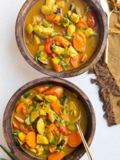 Two wooden bowls of yellow Thai curry soup with chicken and vegetables and gold spoons.