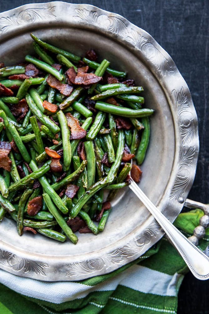 Silver bowl of bacon fried green beans with a silver spoon to the side.