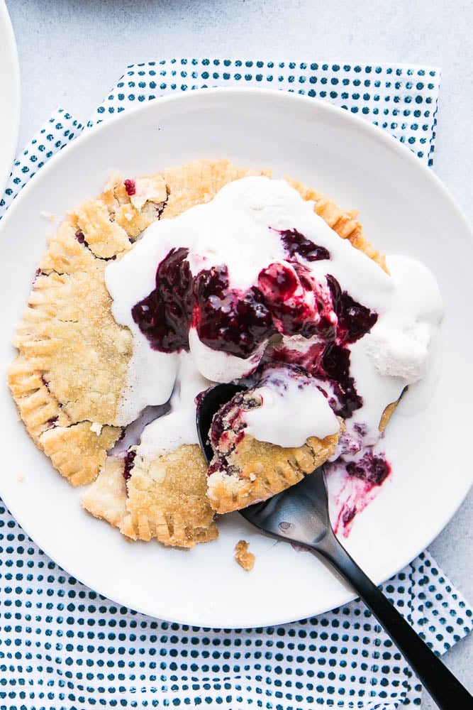Gluten-free berry hand pie on a white plate with whipped cream on top.