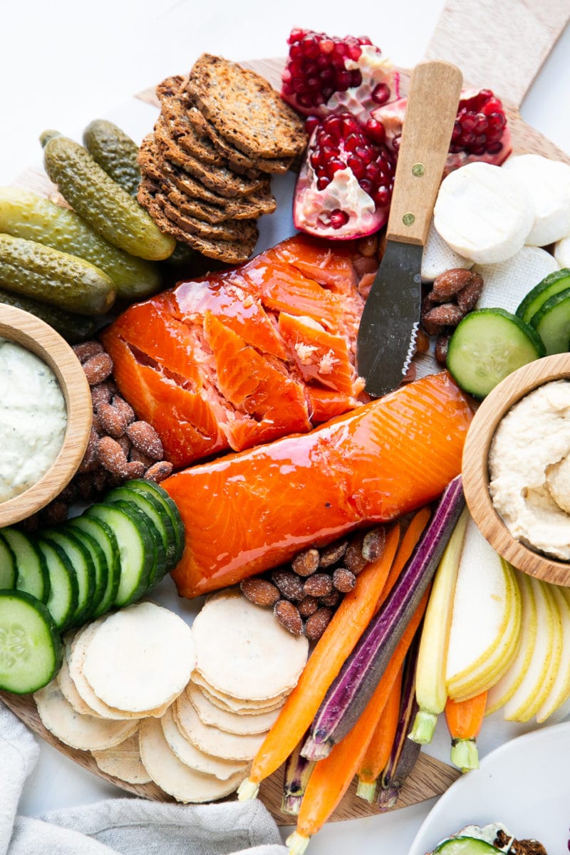 Smoked salmon on a charcuterie board with cheese, crackers, and vegetables