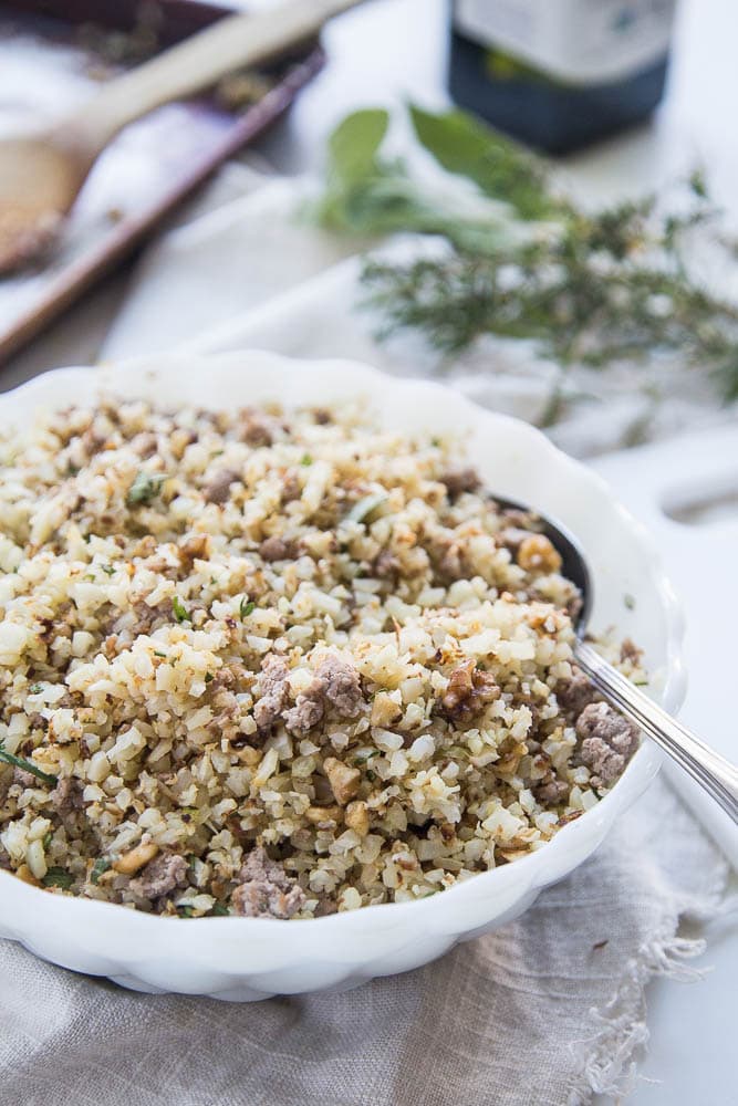 Roasted cauliflower sausage stuffing in a white bowl with a spoon.