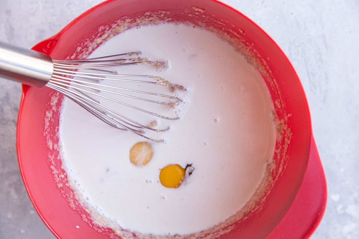 Milk and eggs on top of mashed banana and almond butter in a mixing bowl.