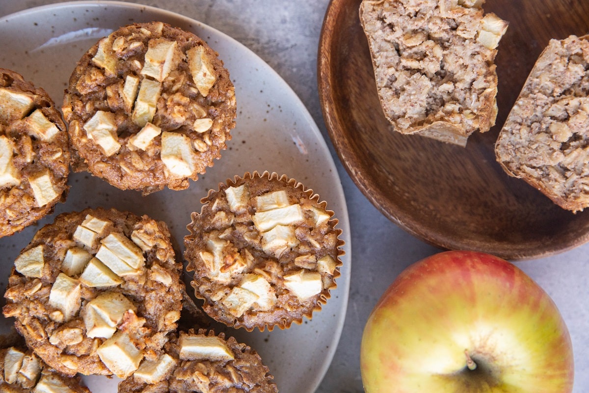 Plate of oatmeal muffins with a plate to the side with a muffin sliced in half so you can see the inside.