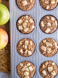 Muffin tray with finished oatmeal muffins and fresh apples to the side.