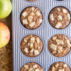 Muffin tray with finished oatmeal muffins and fresh apples to the side.