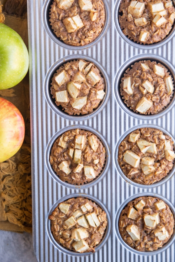 Muffin tray with finished oatmeal muffins and fresh apples to the side.