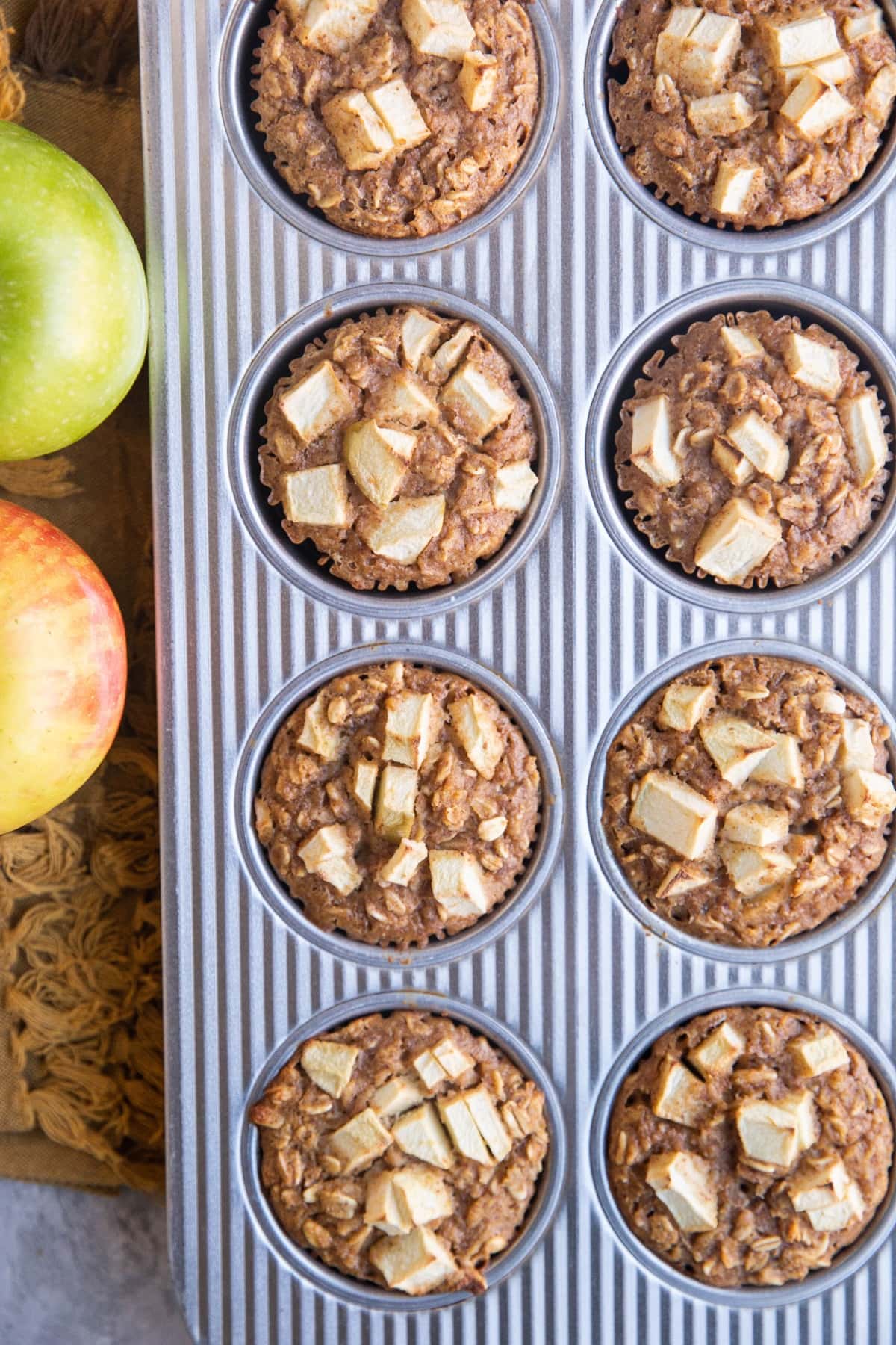 Muffin tray with finished oatmeal muffins and fresh apples to the side.