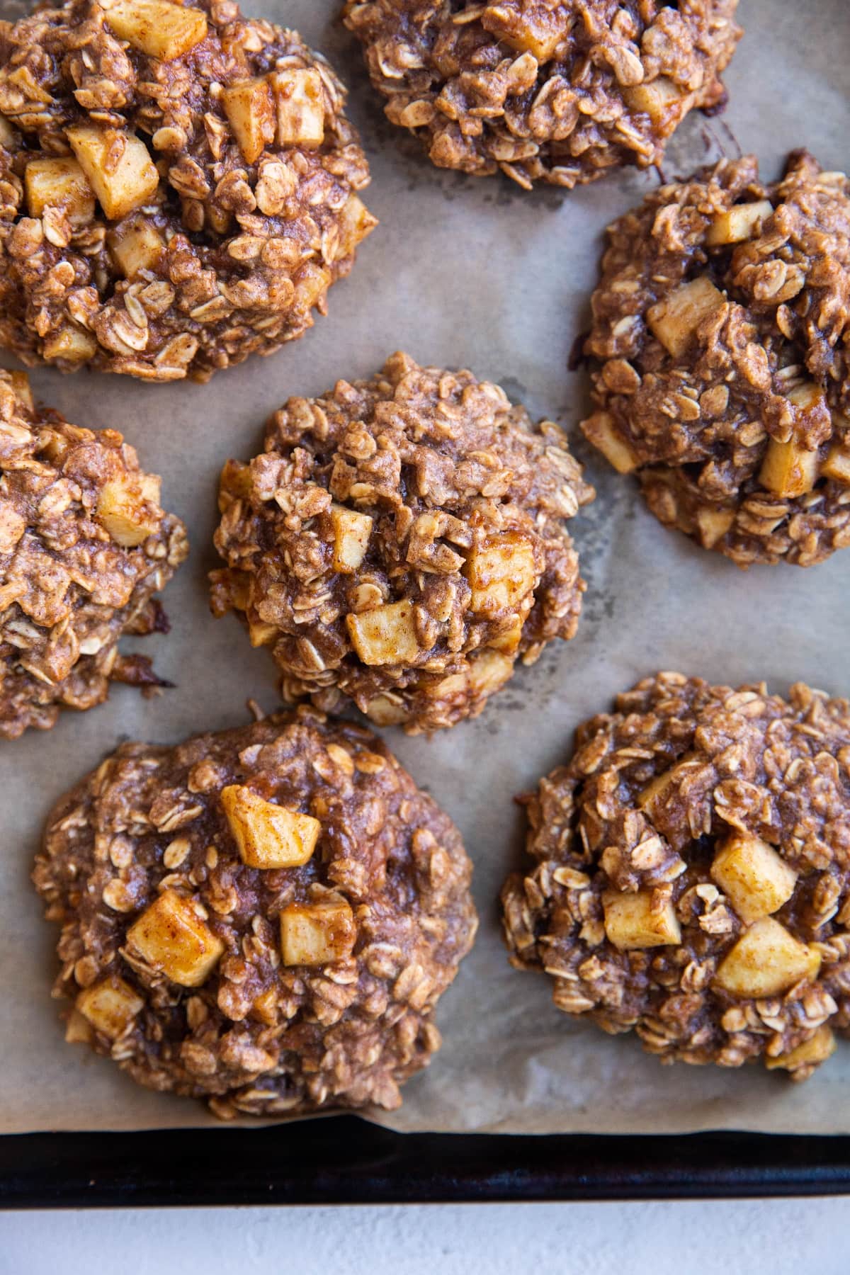 Baking sheet lined with parchment paper with baked apple oatmeal cookies fresh out of the oven.