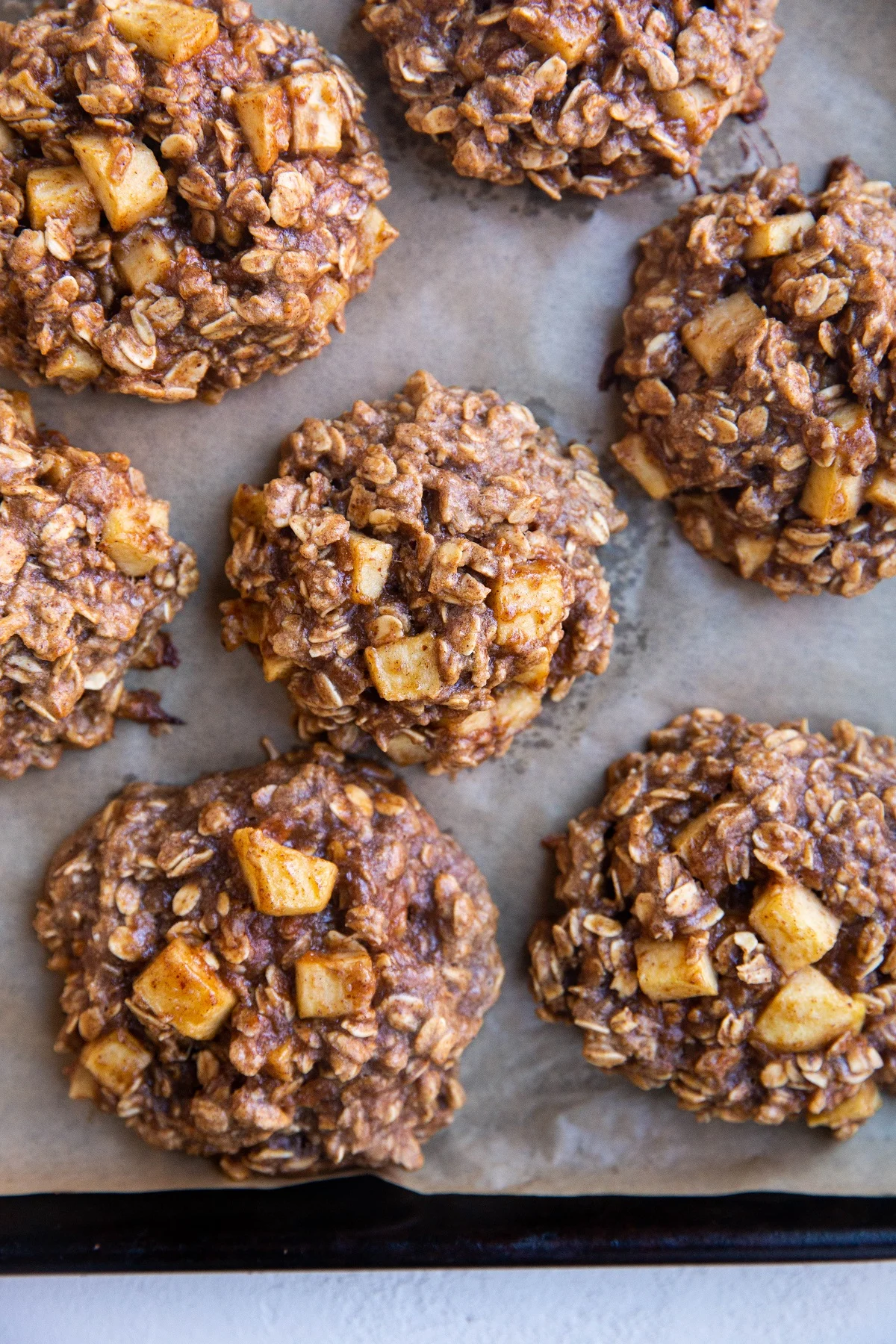 Baking sheet lined with parchment paper with baked apple oatmeal cookies fresh out of the oven.