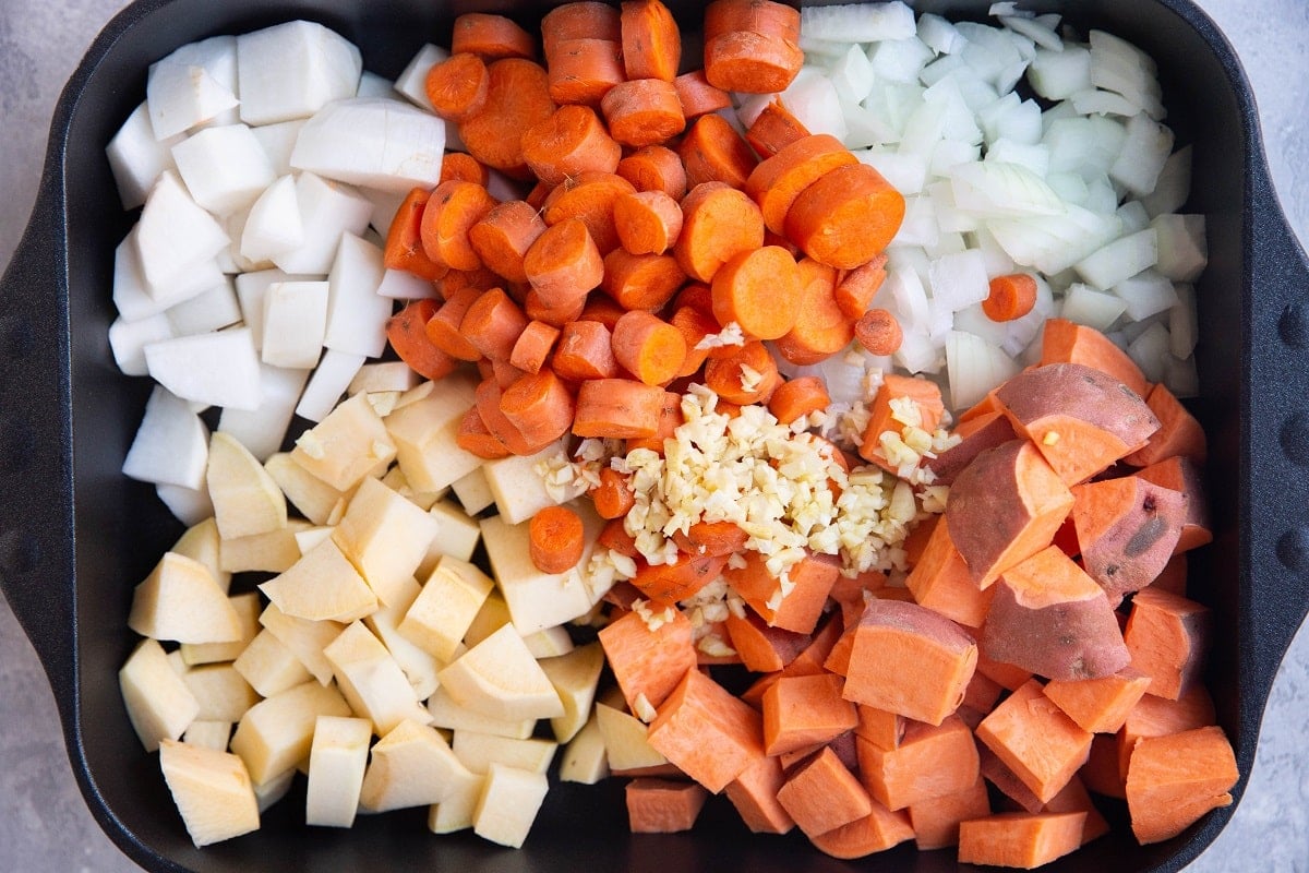 Raw root vegetables in a casserole dish, chopped and ready to be roasted