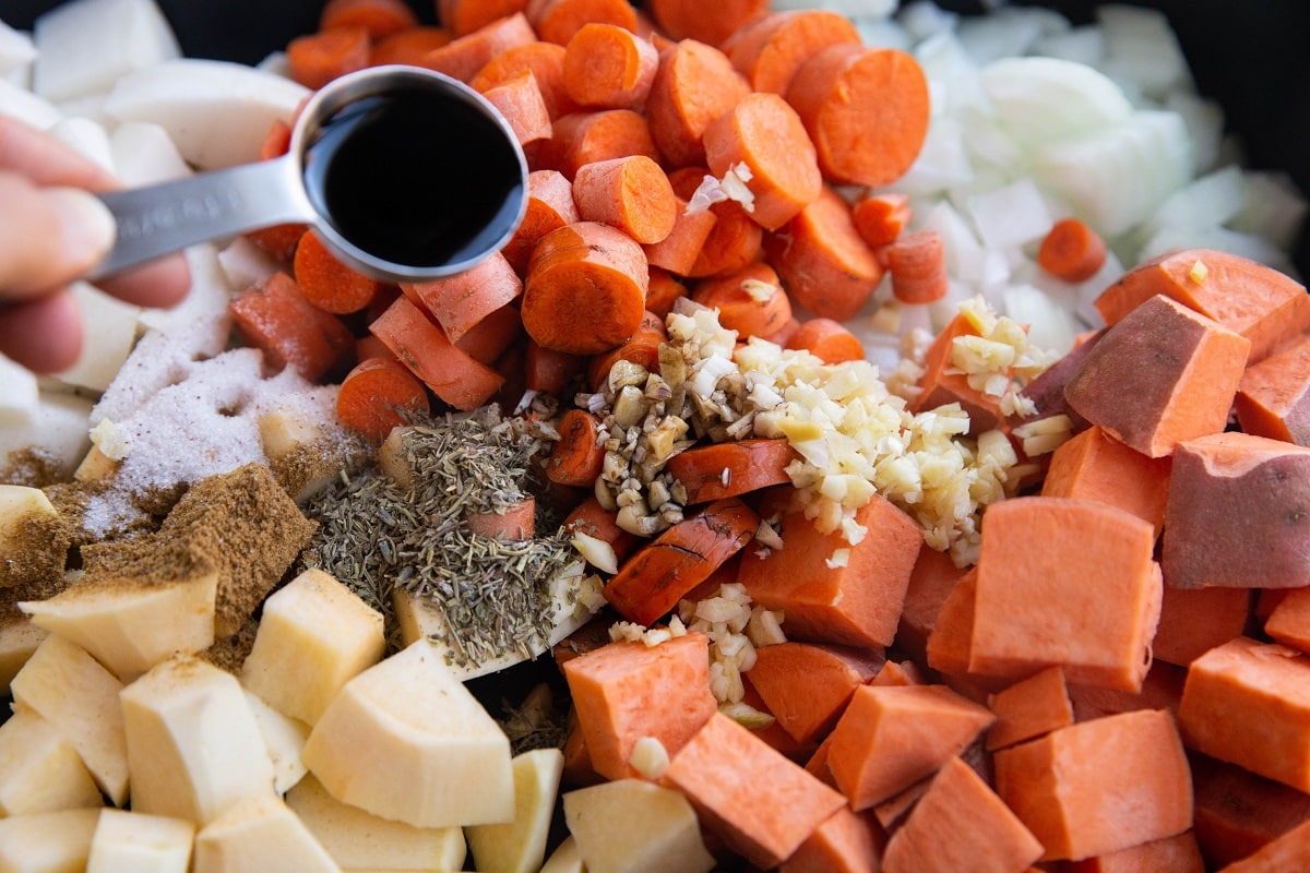 Balsamic vinegar being poured into the casserole dish with the root veggies.