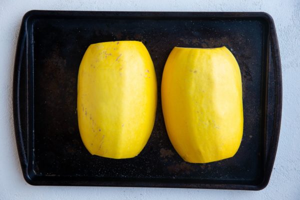 Spaghetti squash halves cut side down on a baking sheet, ready to go into the oven.