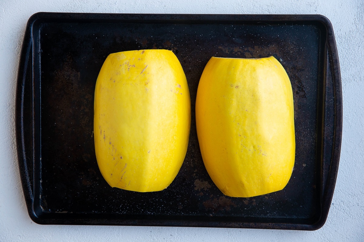 Spaghetti squash halves cut side down on a baking sheet, ready to go into the oven.
