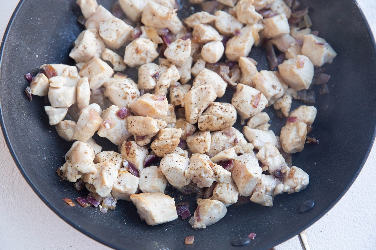 Onions, garlic, and chicken cooking in a skillet.