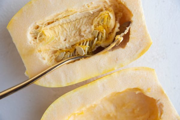 Spaghetti squash halves face up with a spoon scooping out the insides.