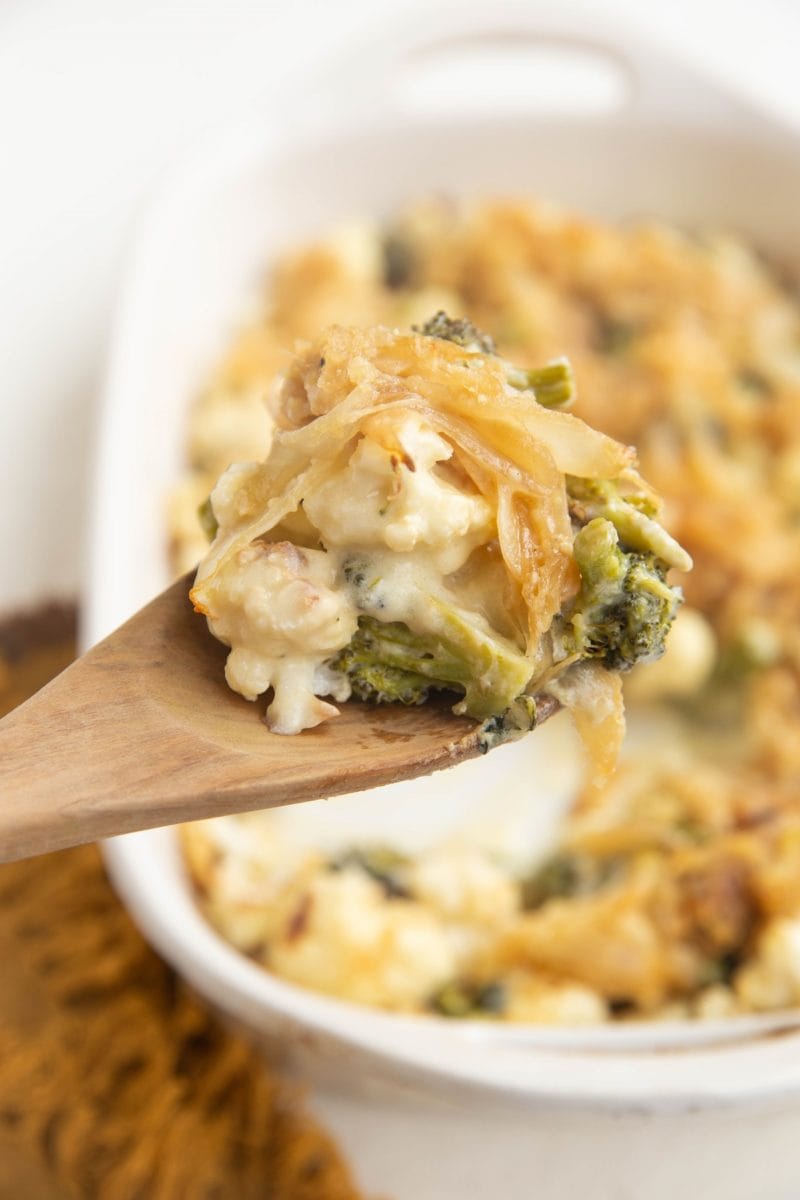 Vertical image of wooden spoon taking a scoop of broccoli casserole.