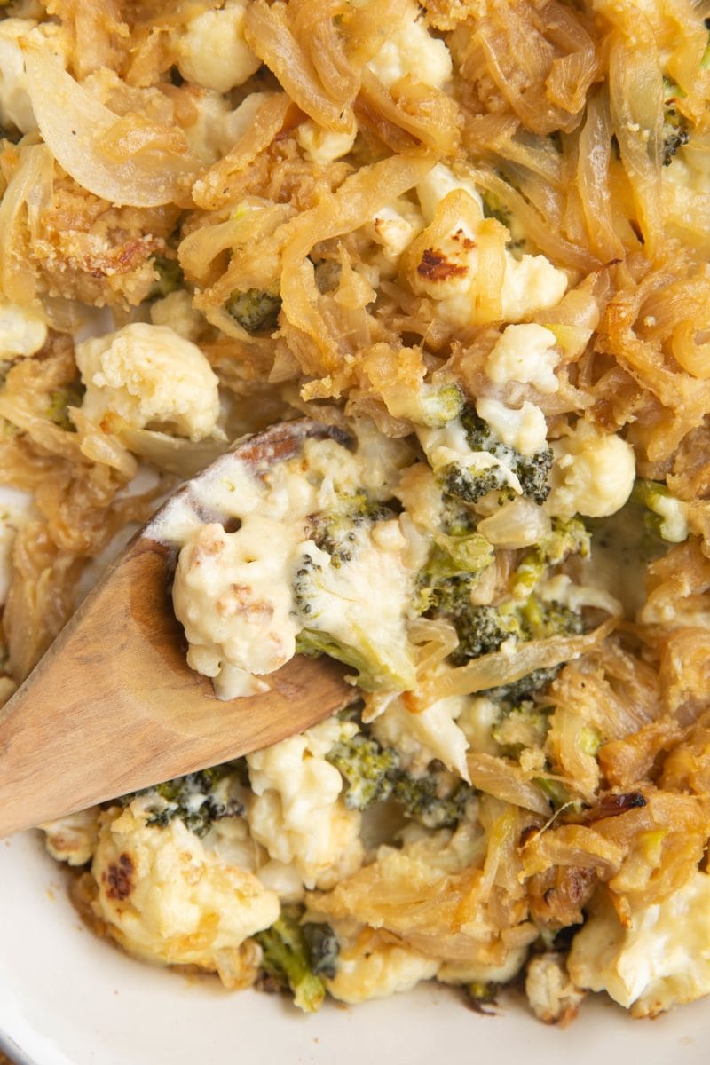 Close up top down image of wooden spoon digging into the cauliflower casserole.