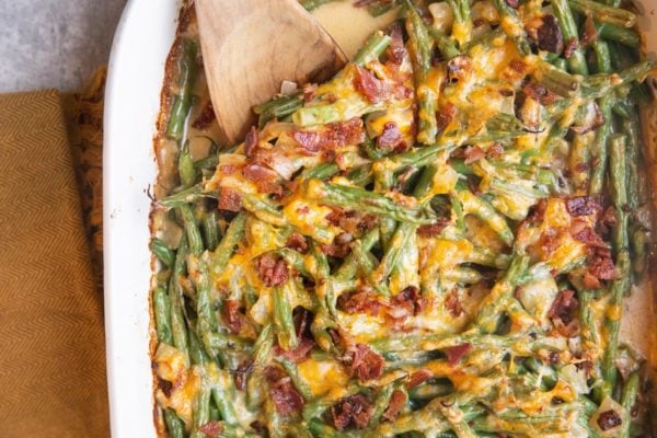 Horizontal photo of finished green bean casserole fresh out of the oven with a wooden spoon inside the casserole.