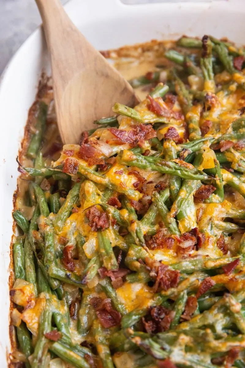 Close up shot of cheesy green bean casserole with bacon in a casserole dish.