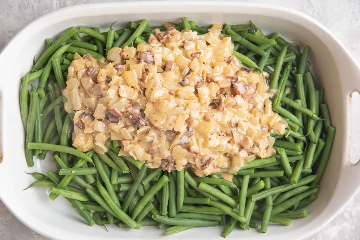 Green beans in a white casserole dish with creamy sauce poured on top.