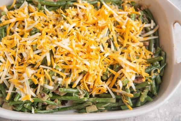 Green beans coated with sauce in a casserole dish with grated cheddar cheese on top.