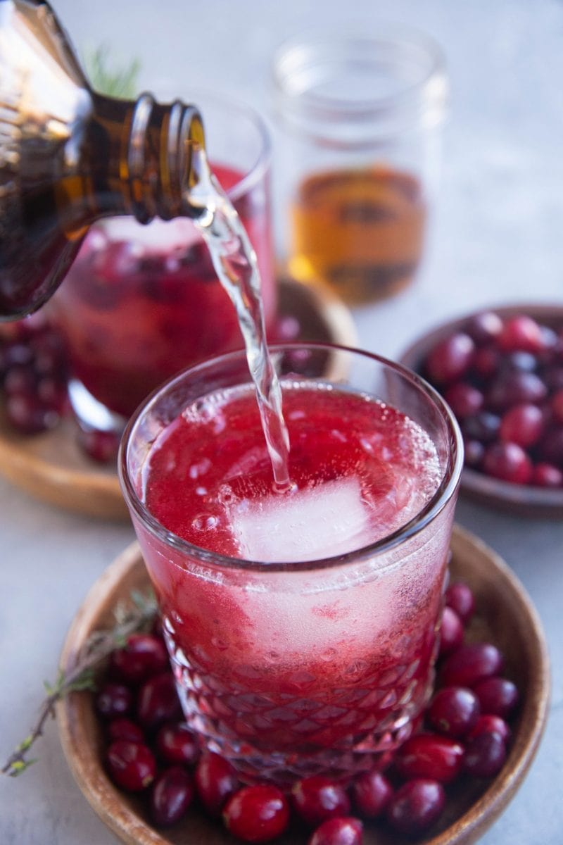 Ginger beer being poured into a glass with cranberry and bourbon.