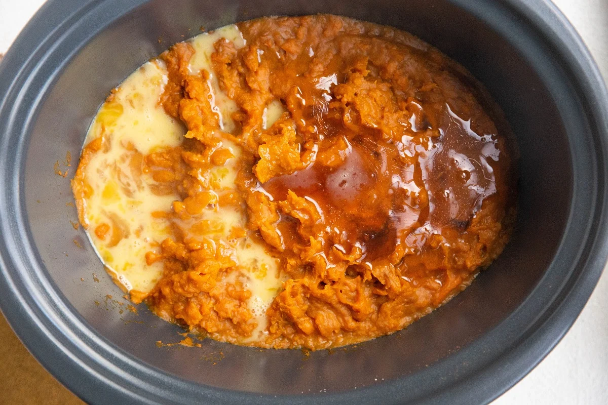 Mashed sweet potatoes, beaten egg, and honey in a crock pot, ready to be mixed up.