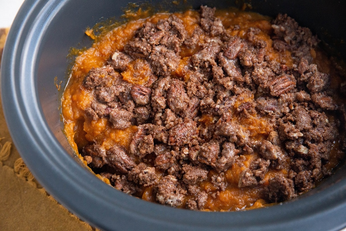 Mashed sweet potatoes in a slow cooker with pecan topping on top, ready to be slow cooked.