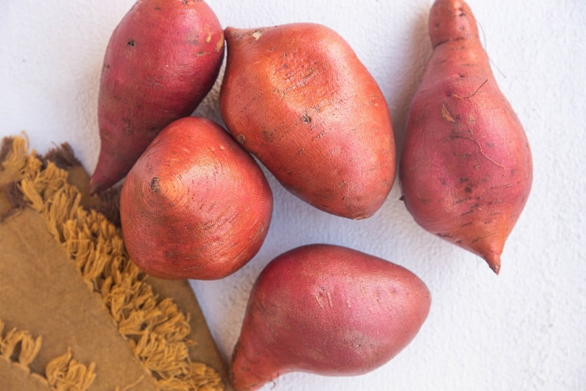 Raw sweet potatoes on a white background with a golden napkin to the side.