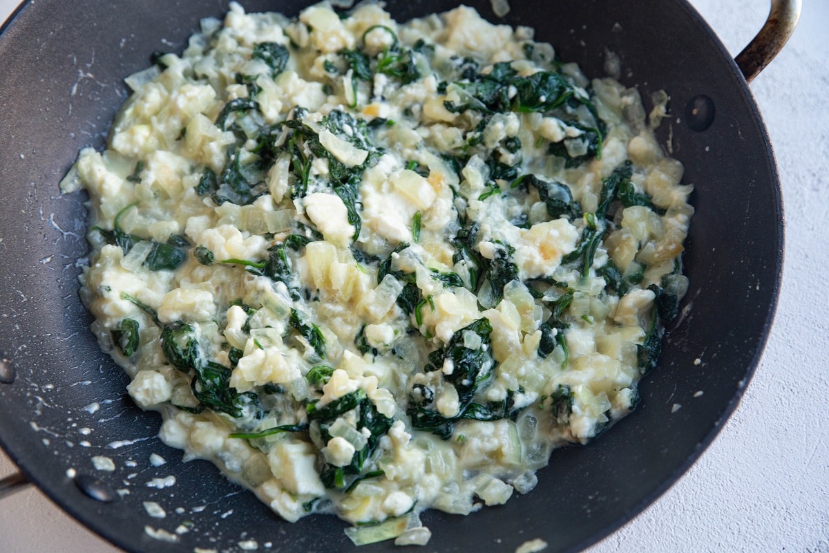 Onions, spinach, garlic, and feta cooking in a skillet
