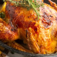 Close up image of cooked Thanksgiving turkey in a black roasting pan with fresh herbs on top.