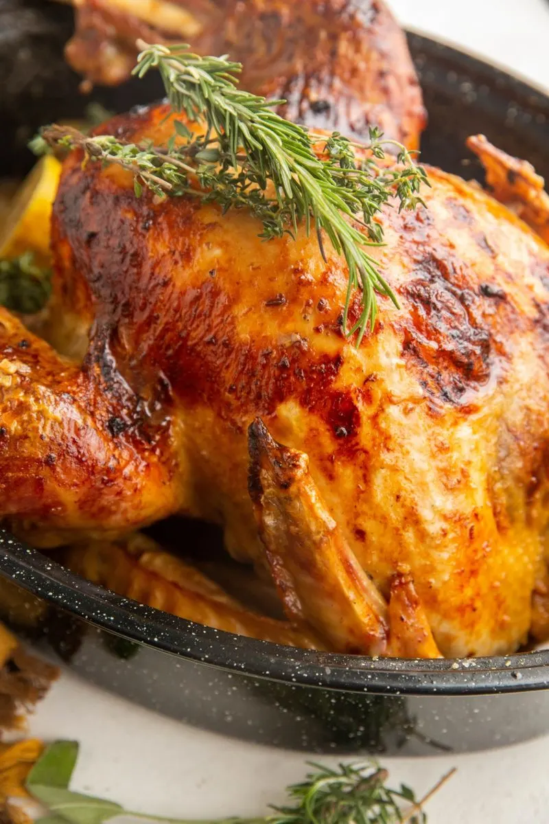 Close up image of cooked Thanksgiving turkey in a black roasting pan with fresh herbs on top.