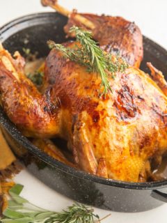 Roast turkey in a roasting pan with fresh herbs on top and fresh herbs to the side.