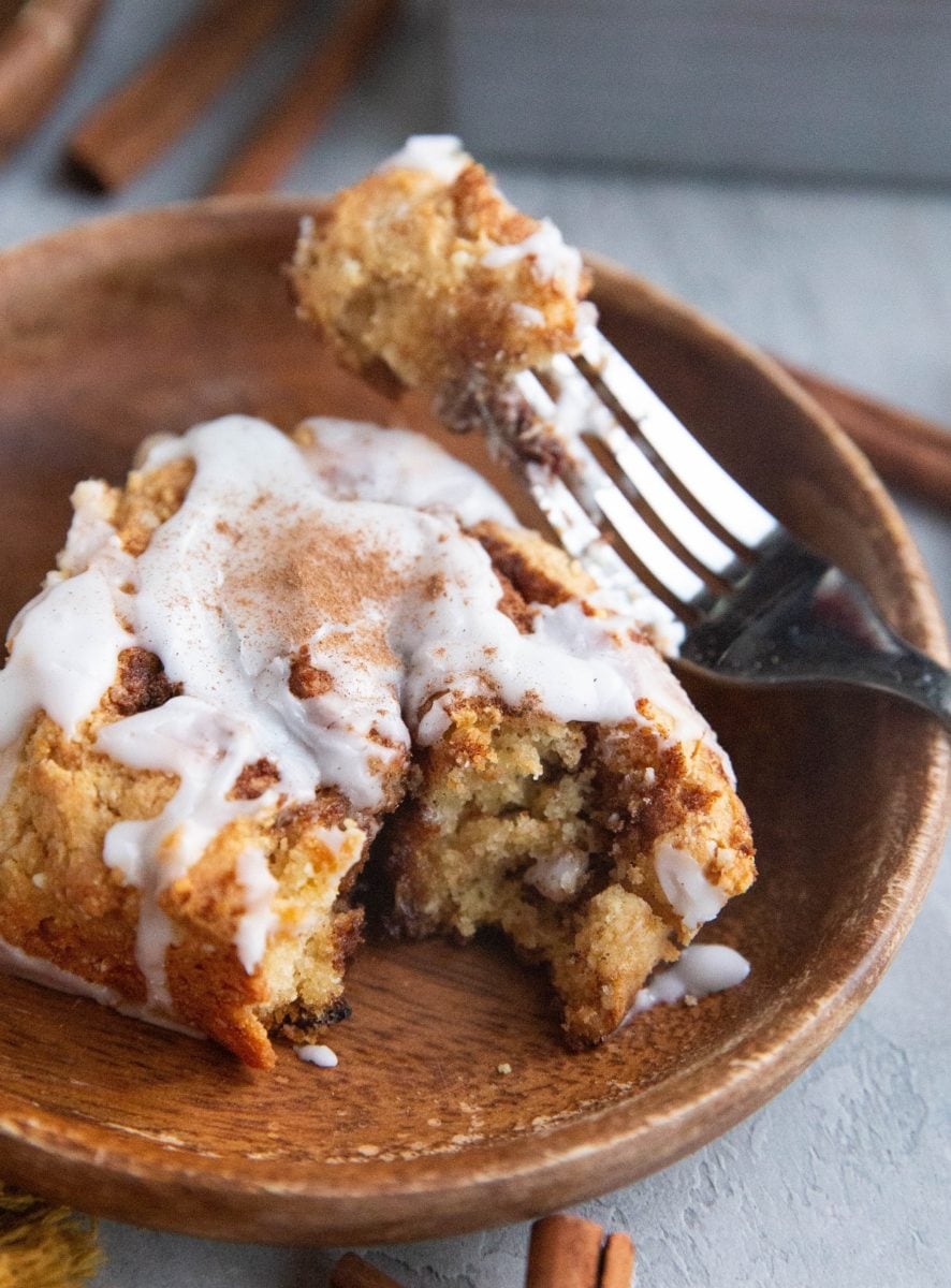 Cinnamon roll on a plate with a bite taken out, exposing the inside of the roll.