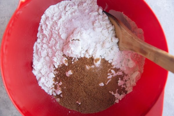 Dry ingredients for cinnamon rolls in a red mixing bowl with a wooden spoon, ready to be mixed together.