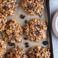 Top down photo of 6-Ingredient Healthy Oatmeal Raisin Cookies on a baking sheet with rogue raisins around the cookies