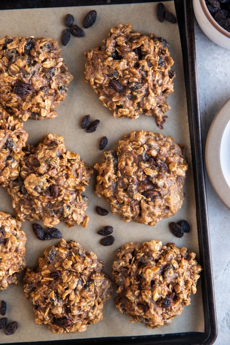 Top down photo of 6-Ingredient Healthy Oatmeal Raisin Cookies on a baking sheet with rogue raisins around the cookies