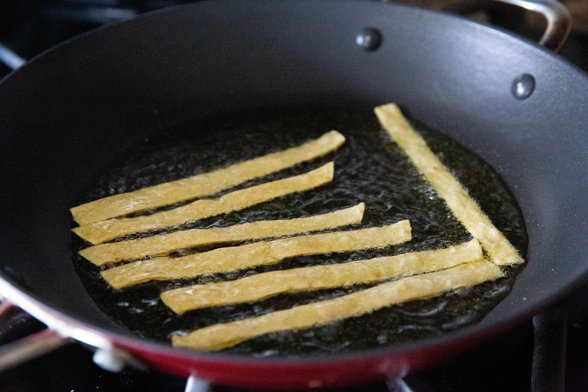 Tortilla strips frying in oil in a skillet.