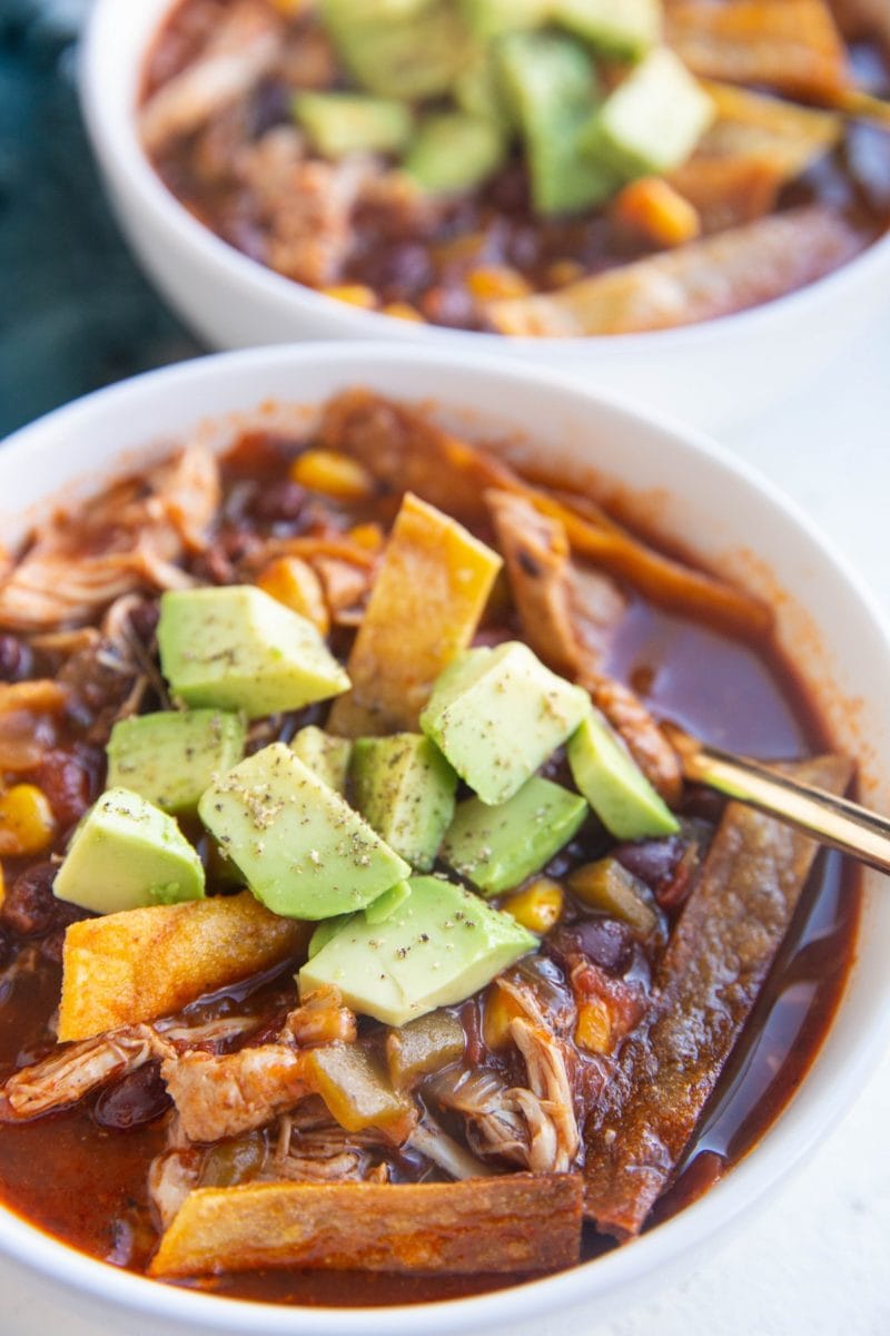 Two bowls of chicken tortilla soup with fresh avocado on top.