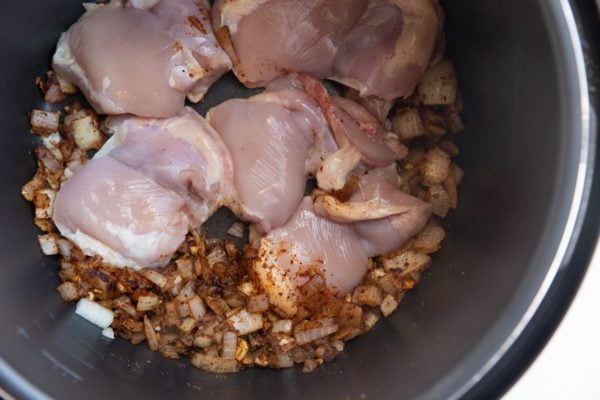 Chicken thighs in a pressure cooker with onions, garlic, and spices.